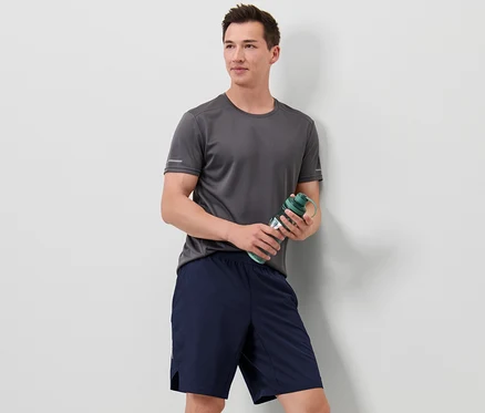 Mann im grauen T-Shirt hält eine grüne Wasserflasche und trägt Sportshorts.