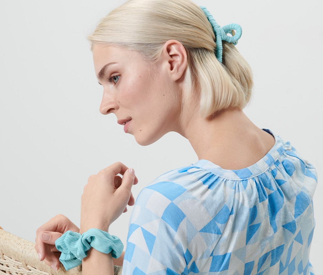 Blonde Frau sitzt im Sessel, trägt ein Haarband am Handgelenk und eine Haarspange im Haar. Haaraccessoires-Set.