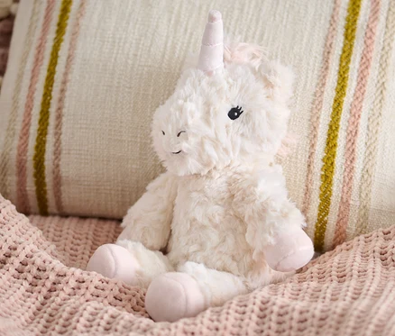 Plüschtier »Einhorn« sitzt auf einer rosa Strickdecke neben einem beigen Kissen.