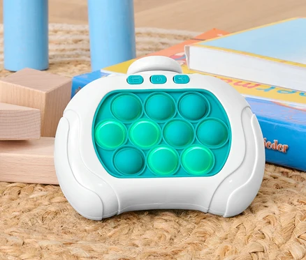 Pop-it-Spiel liegt auf einer Unterlage zwischen Holzbausteinen und Büchern.