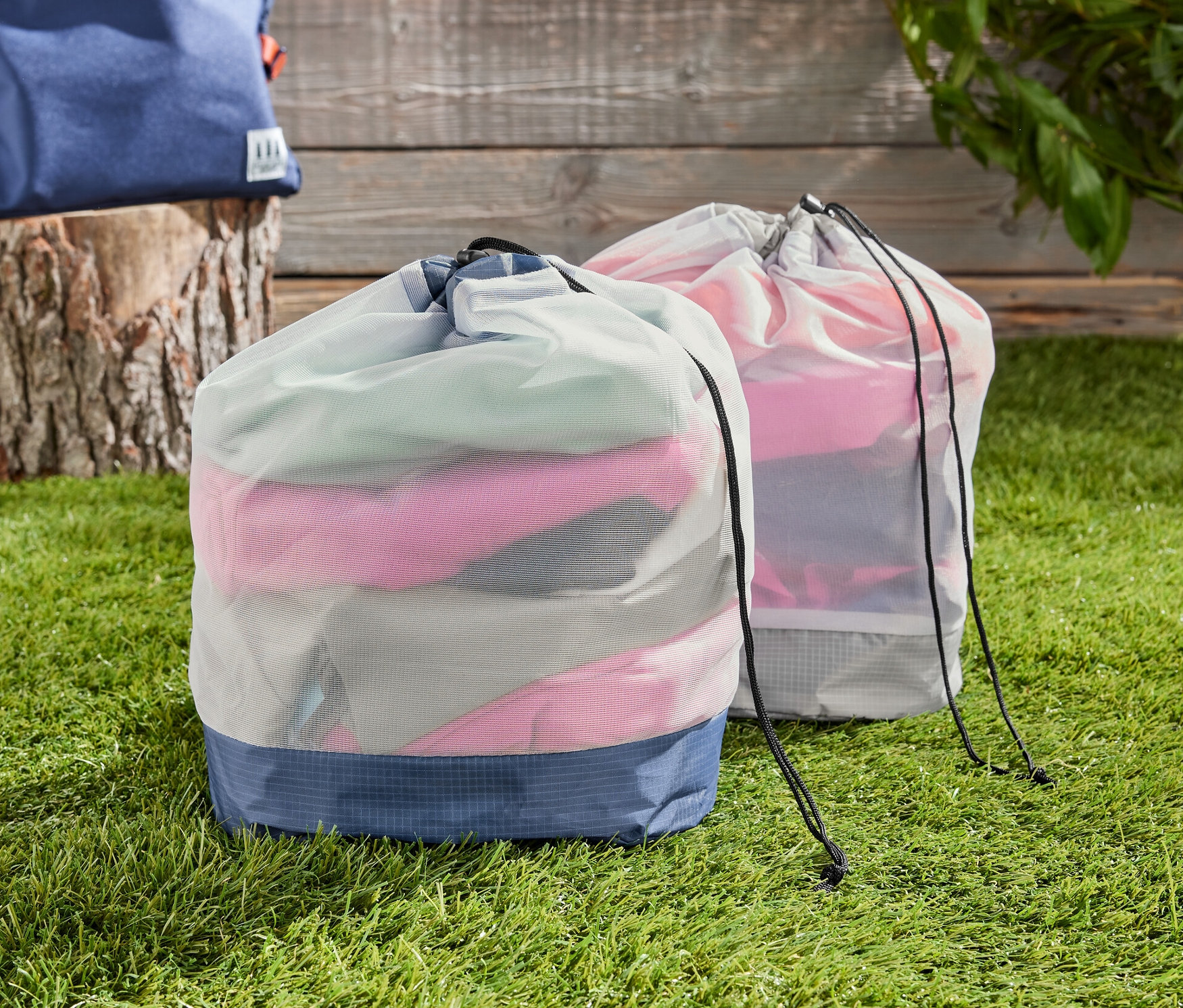 Zwei Outdoor-Meshbeutel auf einer Wiese, im Hintergrund ein Rucksack.