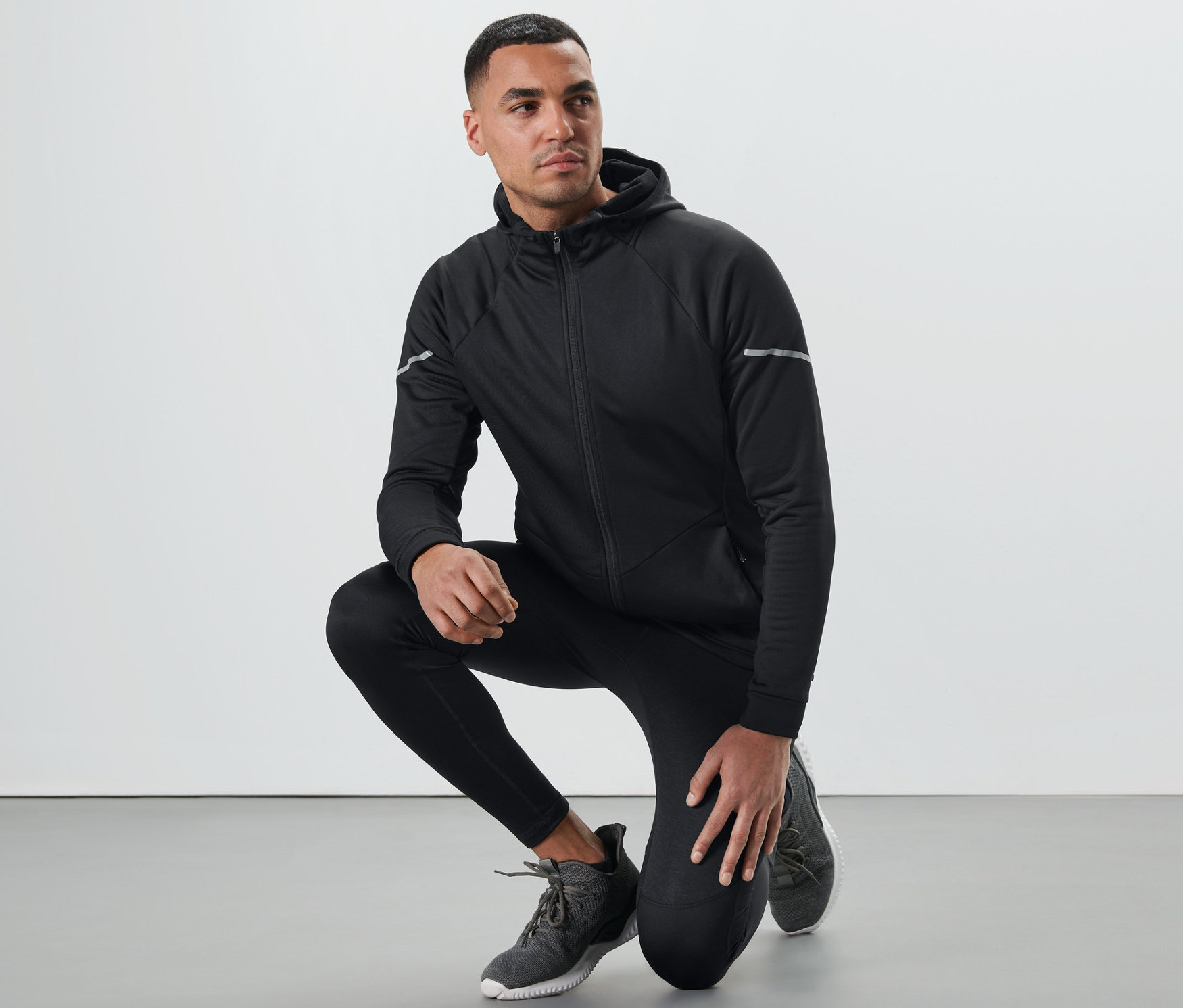 Mann in schwarzer Thermojacke kniet.