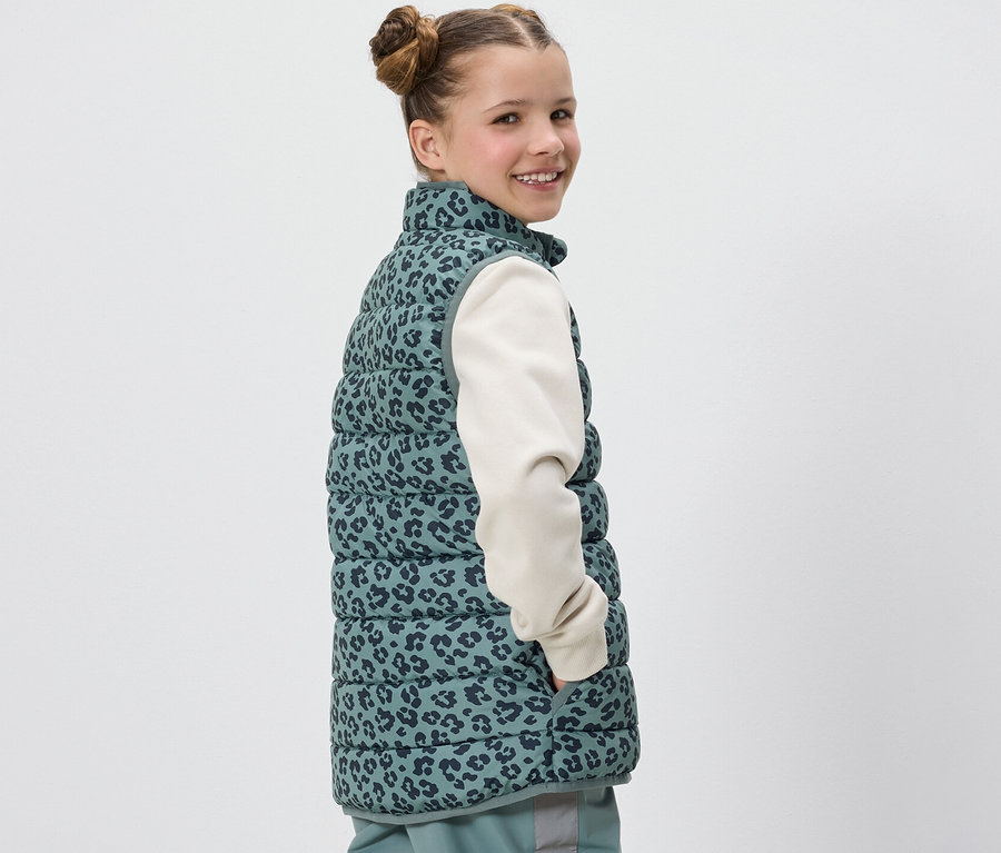 Mädchen lächelt über die Schulter und trägt eine Kinder-Steppweste mit Leopardenmuster.
