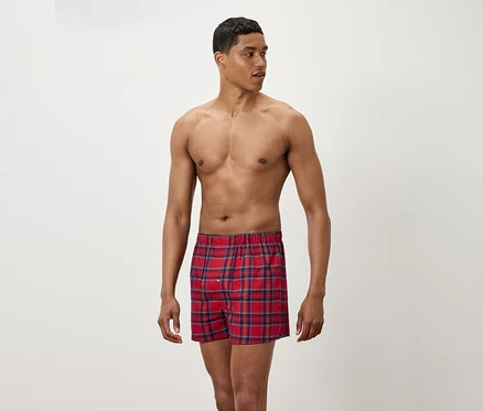 Mann mit freiem Oberkörper trägt rot karierte Boxershorts.