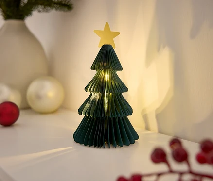 Dekorativer Papierweihnachtsbaum mit Stern auf einem weißen Tisch, beleuchtet mit Lichtern.