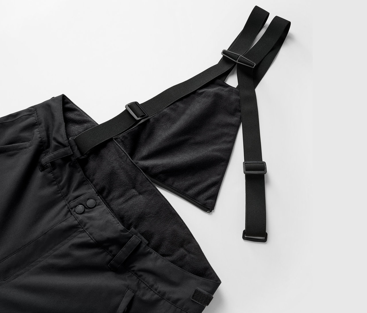 Detailaufnahme einer schwarzen Hose mit Latz und verstellbaren Trägern.