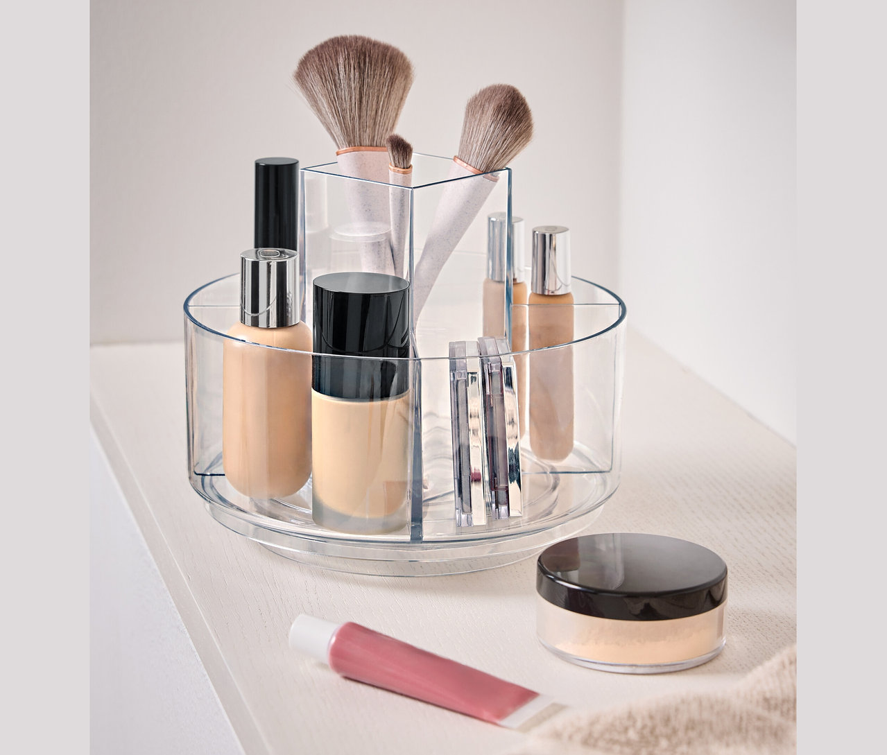 Durchsichtiger, drehbarer Behälter mit Kosmetika auf einer weißen Oberfläche.