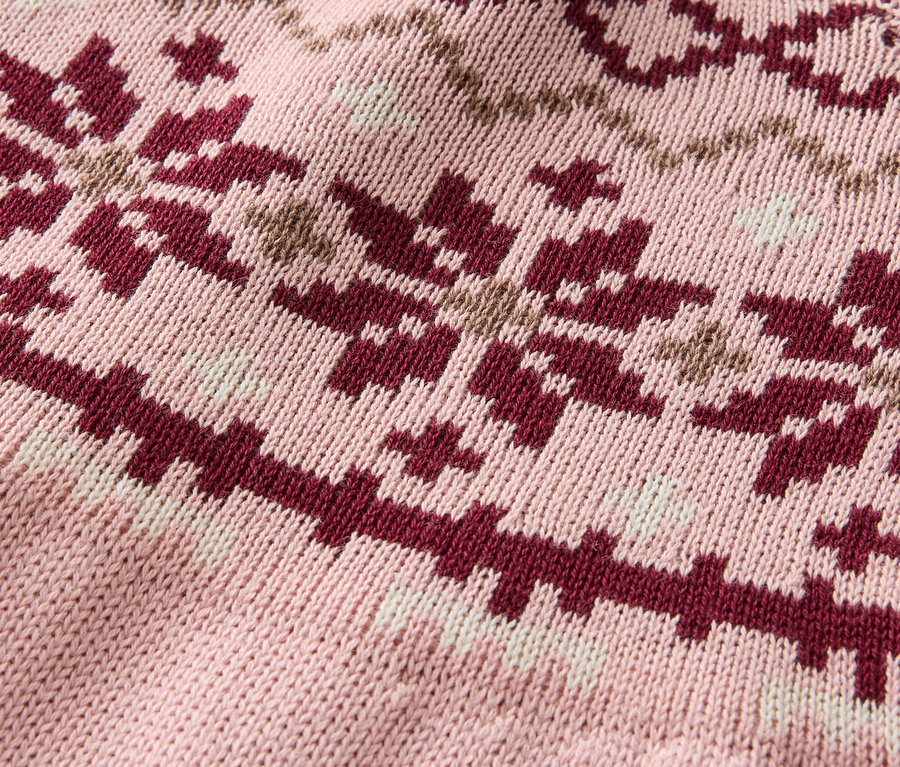 Detailaufnahme eines rosafarbenen Strickpullovers mit einem Muster aus bordeauxroten und beigen Schneeflocken.