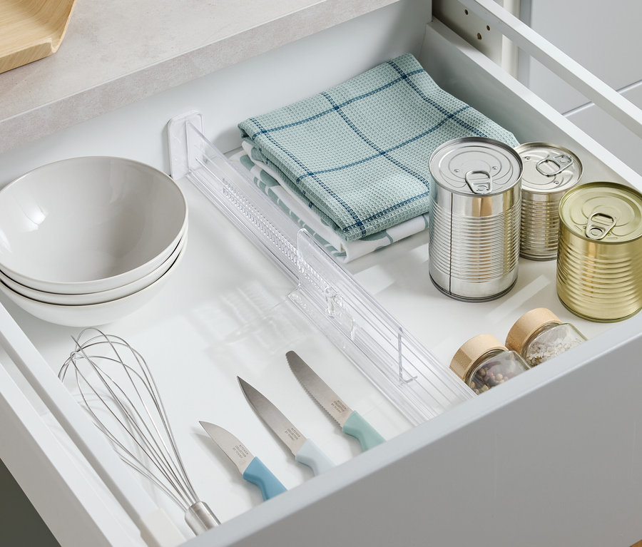 Draufsicht auf eine geöffnete Schublade mit Schüsseln, Geschirrtuch, Konservendosen, Gewürzen, Messern und Schneebesen.