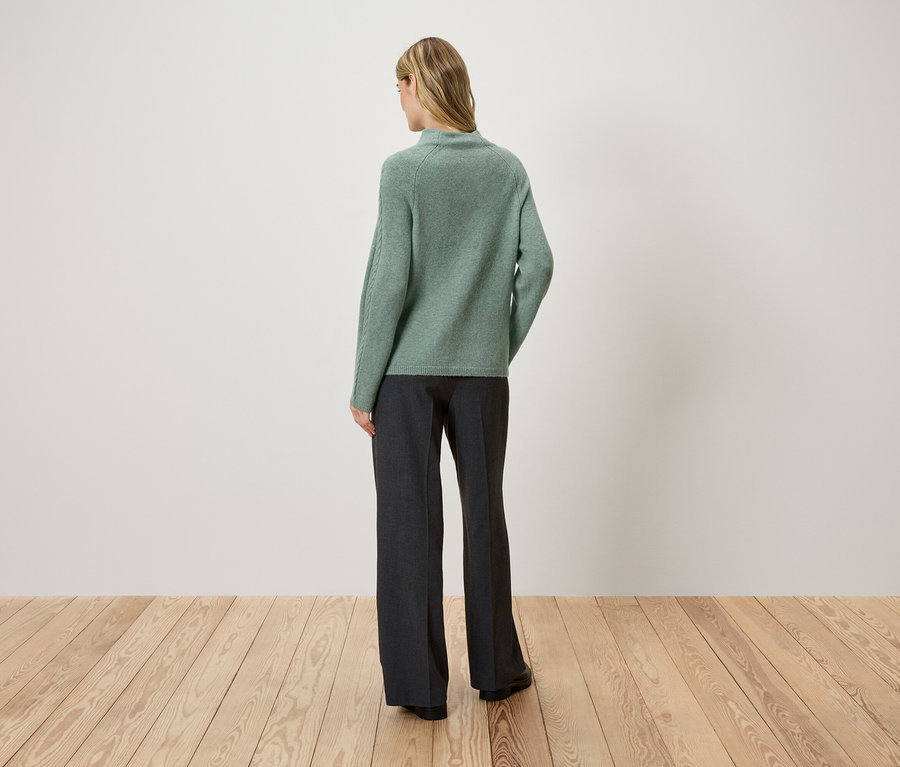 Frau mit dem Rücken zur Kamera trägt einen grünen Pullover und eine dunkle Hose.