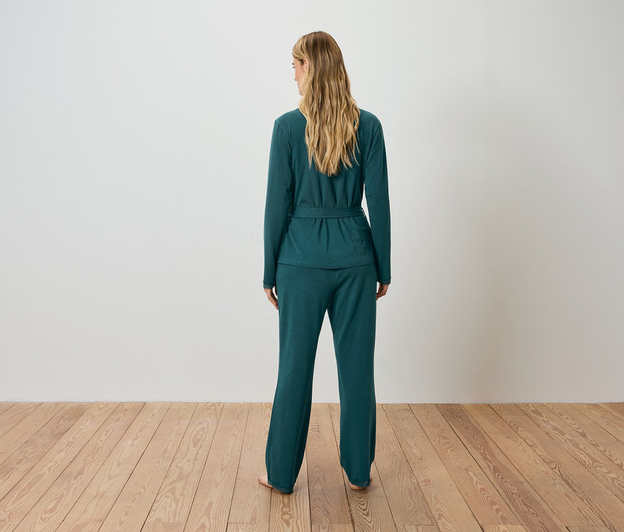 Frau steht mit dem Rücken zur Kamera und trägt einen grünen Cardigan und eine Hose.