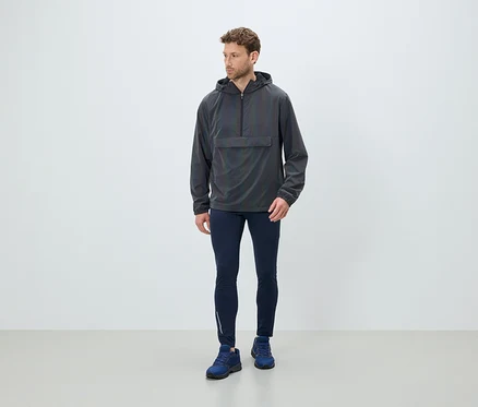 Mann steht und trägt eine graue Kapuzenjacke, dunkelblaue Leggings und blaue Schuhe.