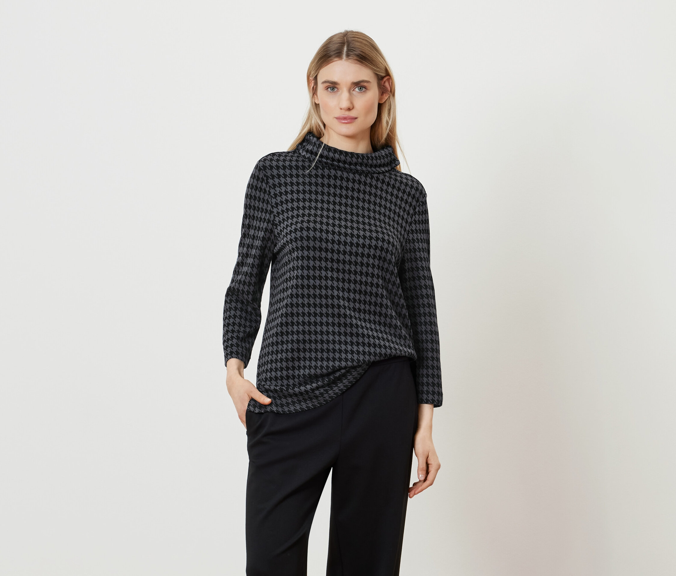 Frau posiert in einem Hahnentrittmuster-Top und einer schwarzen Hose.