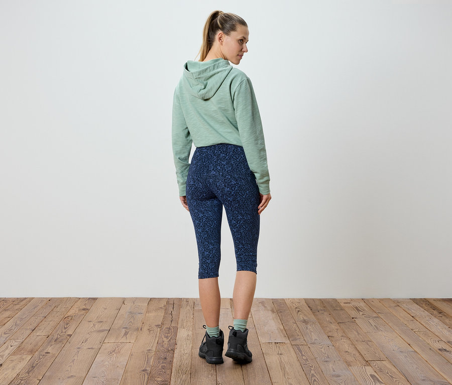 Eine Frau steht mit dem Rücken zur Kamera, trägt einen mintgrünen Kapuzenpullover und marineblaue Leggings mit Blumenmuster.