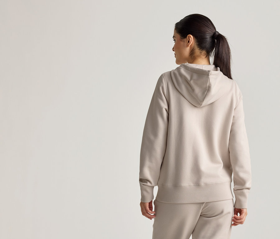 Rückansicht einer Frau mit Pferdeschwanz, die einen beigen Hoodie und eine passende Hose trägt.