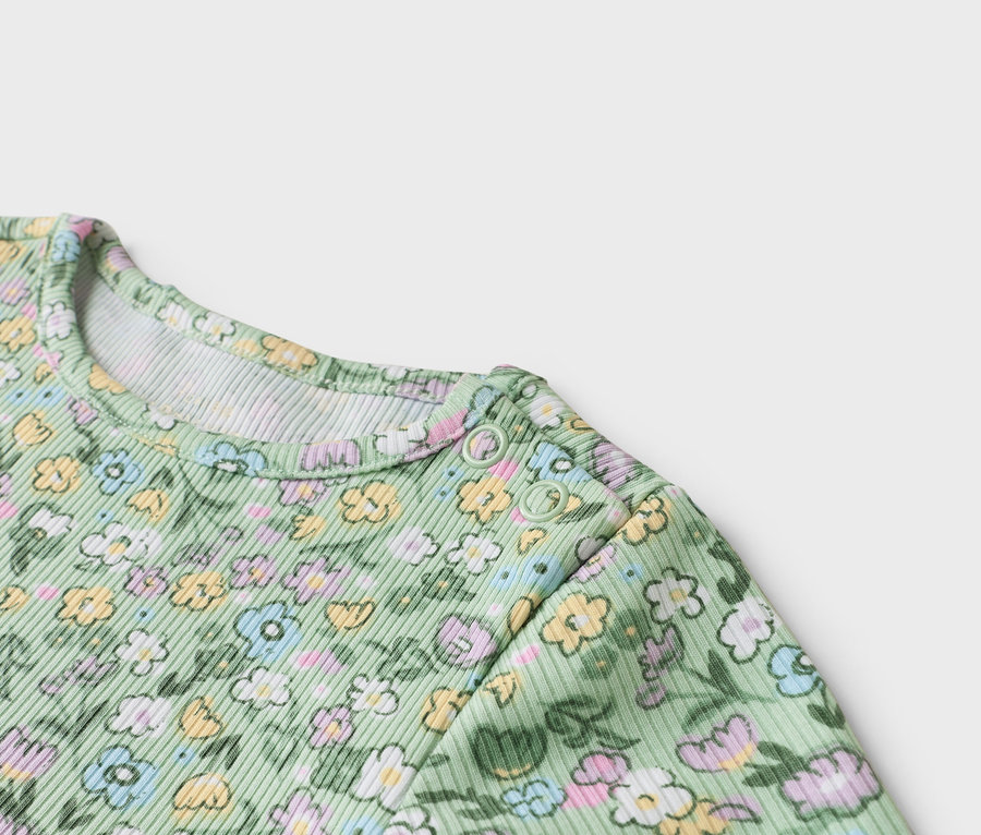 Nahaufnahme eines hellgrünen Babybodys mit Blumenmuster und Druckknöpfen an der Schulter.
