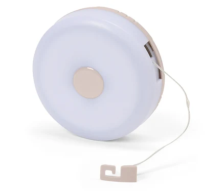 Nahaufnahme einer runden, hellrosa Nachttischlampe mit Zugschnur auf einem weißen Hintergrund.