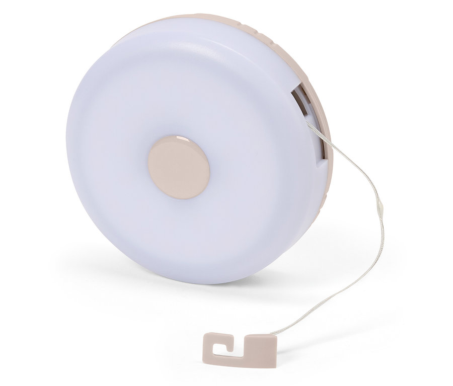 Nahaufnahme einer runden, hellrosa Nachttischlampe mit Zugschnur auf einem weißen Hintergrund.