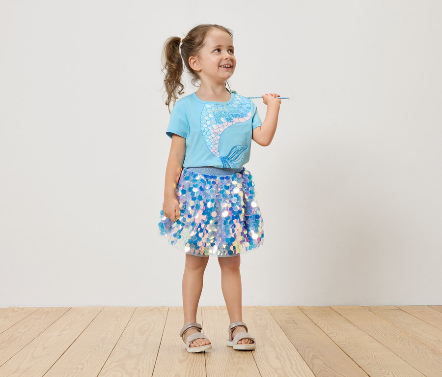Mädchen mit Zöpfen, hellblauem Meerjungfrauen-T-Shirt und blauem Paillettenrock, das einen Zauberstab hält.