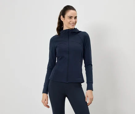 Frau mit Pferdeschwanz trägt marineblaue Jacke mit Kapuze und Leggings vor einem weißen Hintergrund.