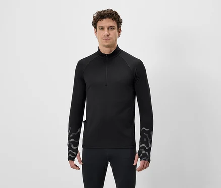 Ein Mann mit lockigem Haar trägt ein schwarzes, langärmeliges Shirt mit Reißverschluss und Leggings vor einem weißen Hintergrund.