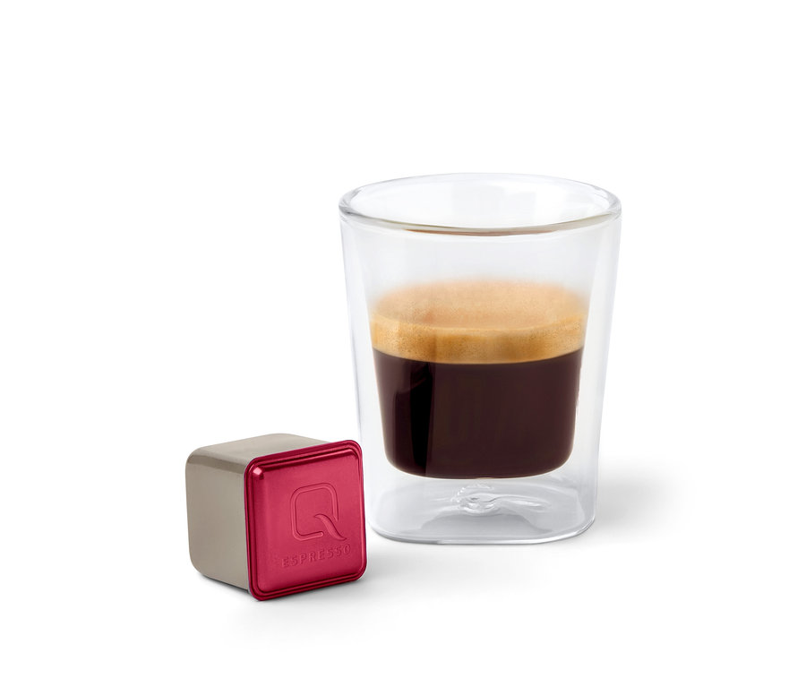 Auf einem weißen Hintergrund steht ein Glas Espresso neben einer Kapsel Qbo Espresso SIDAMA ROYAL.