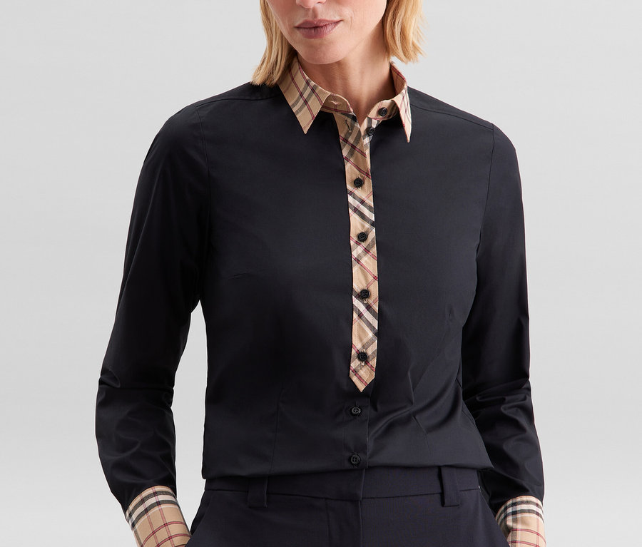 Frau trägt eine schwarze Seidensticker Popeline-Bluse mit Karodetail an Kragen, Knopfleiste und Manschetten, dazu dunkle Hose.