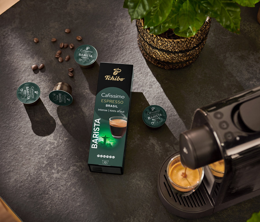 Espressomaschine füllt Tasse. Im Hintergrund Packung Cafissimo BARISTA Espresso Brasil - 10 Kapseln und Kaffeebohne.