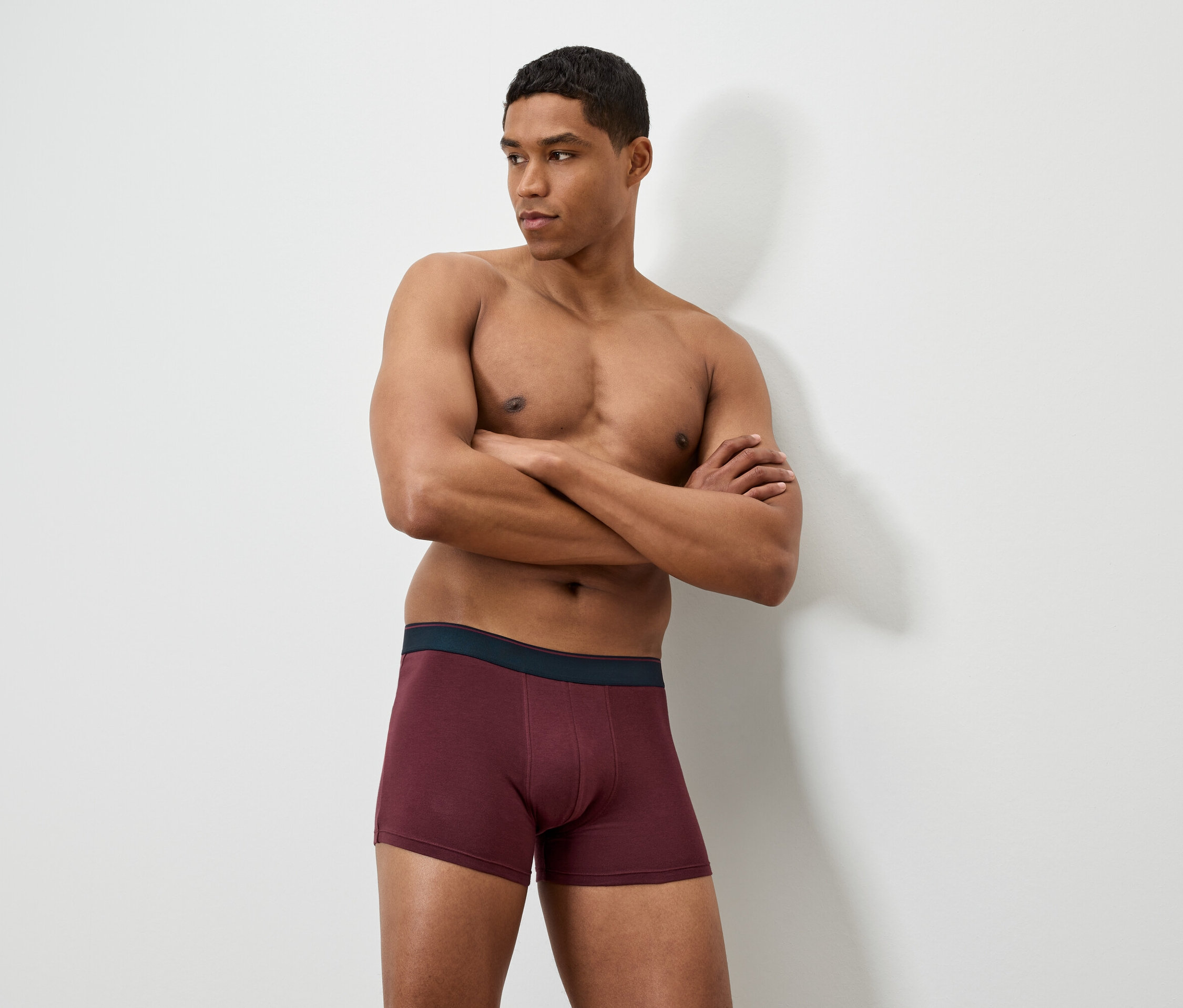 Mann mit verschränkten Armen trägt bordeauxfarbene Boxershorts.