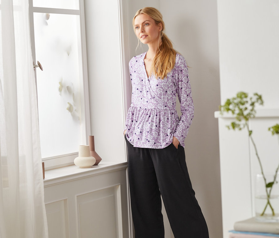 Frau steht am Fenster und trägt ein Langarmshirt.