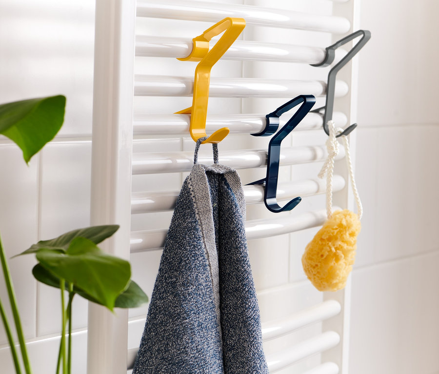 Drei mehrfarbige Clip-Haken hängen an einem Heizkörper. An einem gelben Haken hängt ein Handtuch, an einem blauen ein Schwamm.