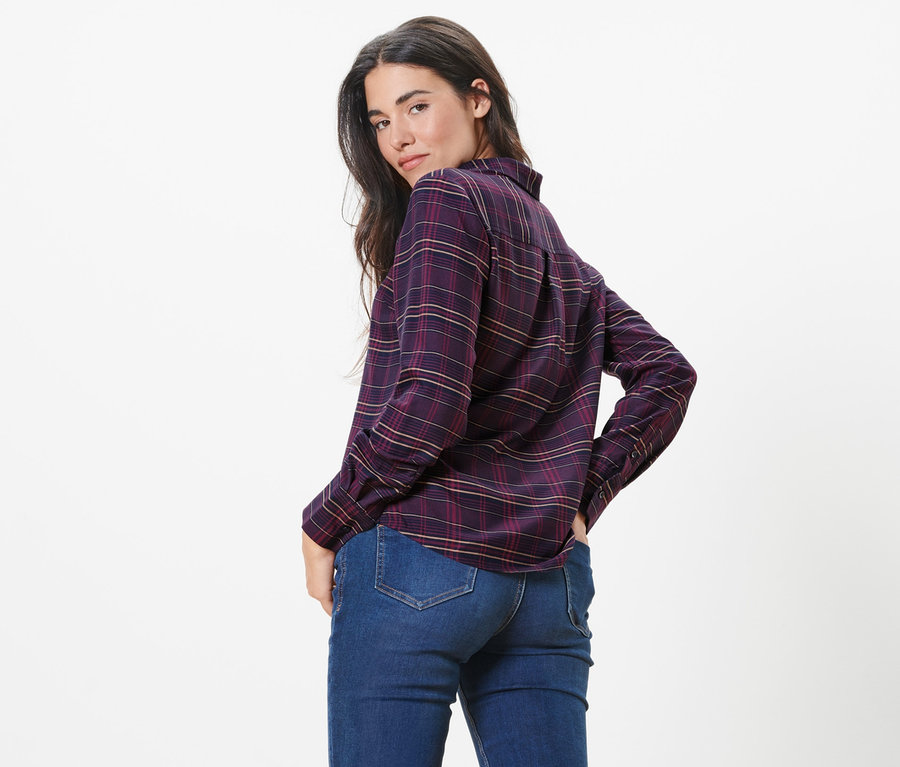 Frau posiert in karierter Hemdbluse und Jeans.