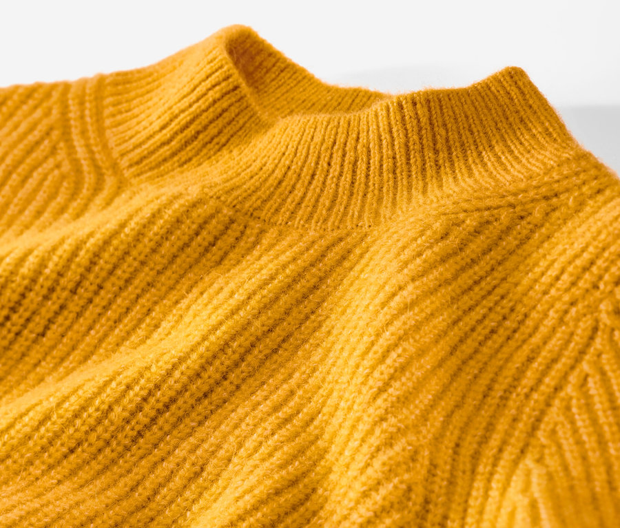 Detailansicht eines gelben Grobstrickpullovers.