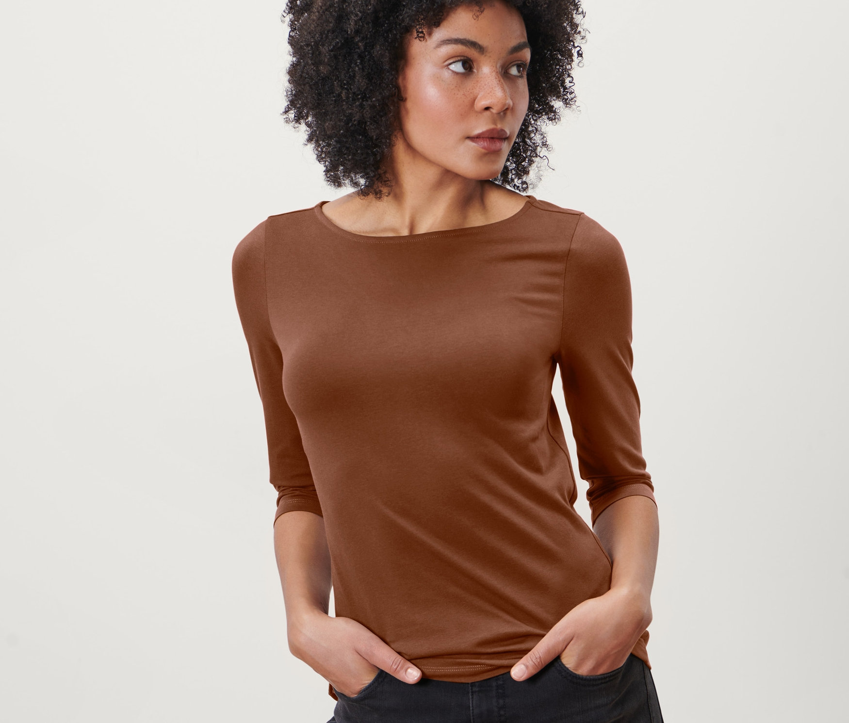 Frau mit Afro-Frisur posiert in einem cognacfarbenen Shirt mit 3/4-Arm.