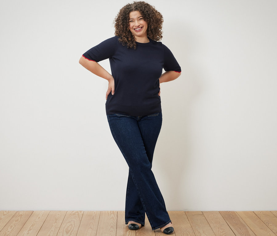 Frau posiert in dunkelblauem Feinstrickpullover und Flared Jeans – Fit »Cara«.