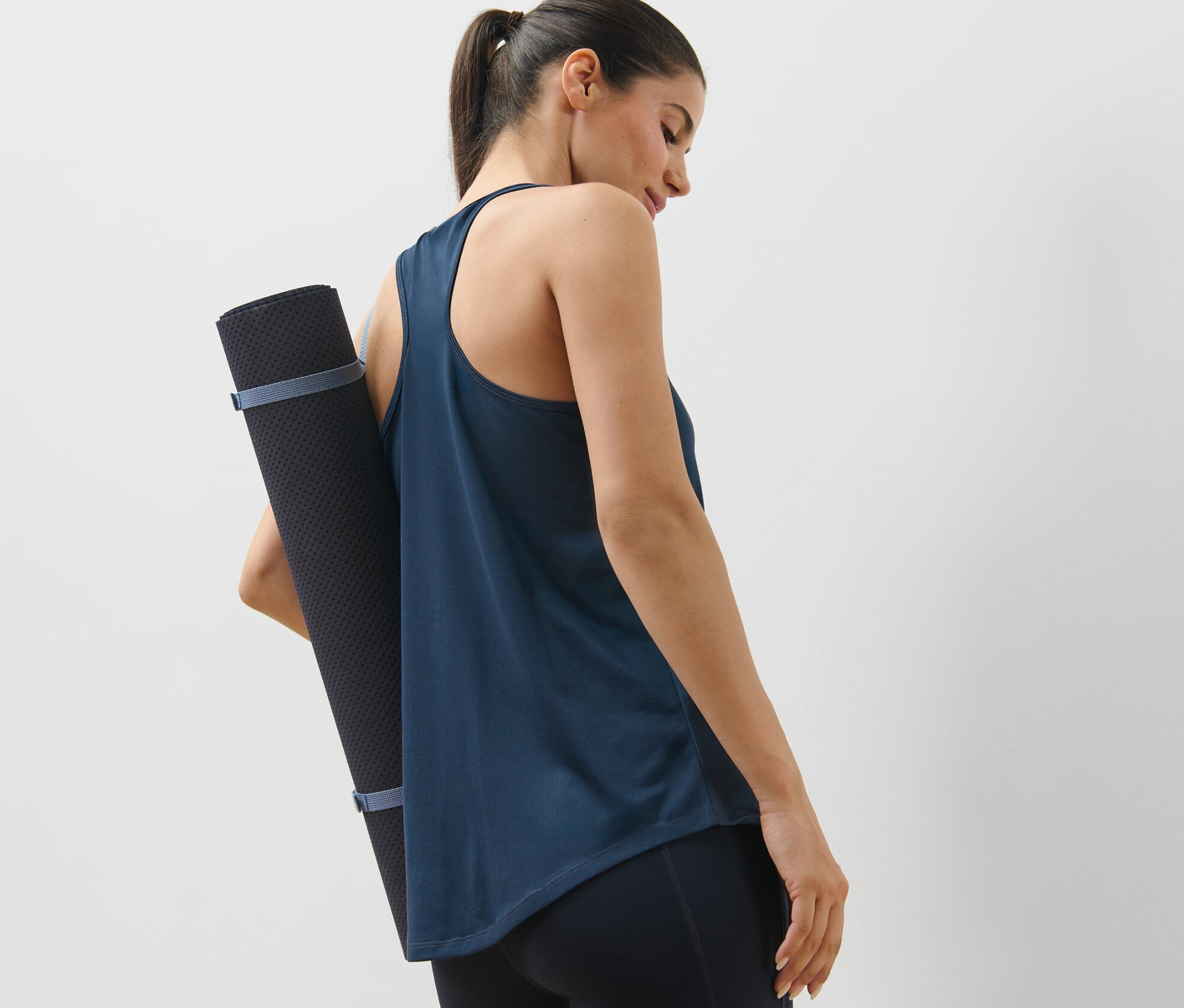 Frau trägt eine Yogamatte in einem blauen 2 Sport-Tops, blau und dunkelblau.