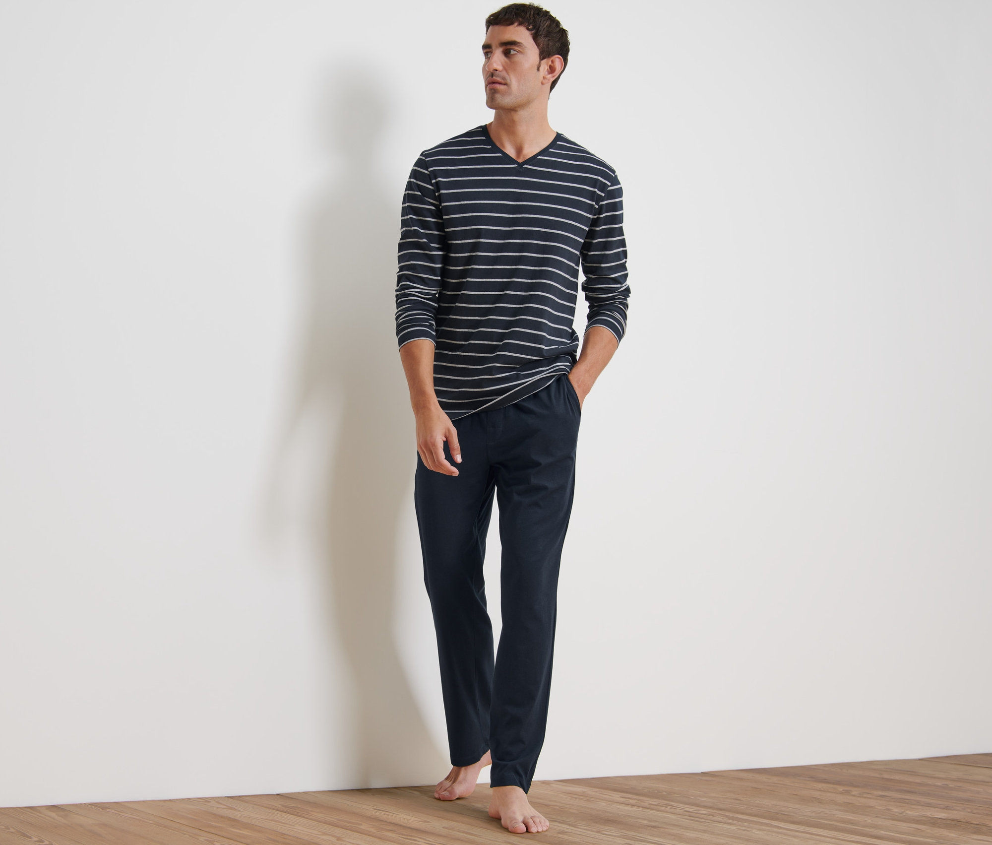 Mann steht und trägt einen Pyjama. Es besteht aus einem langärmligen, gestreiften Oberteil und einer marineblauen Hose.