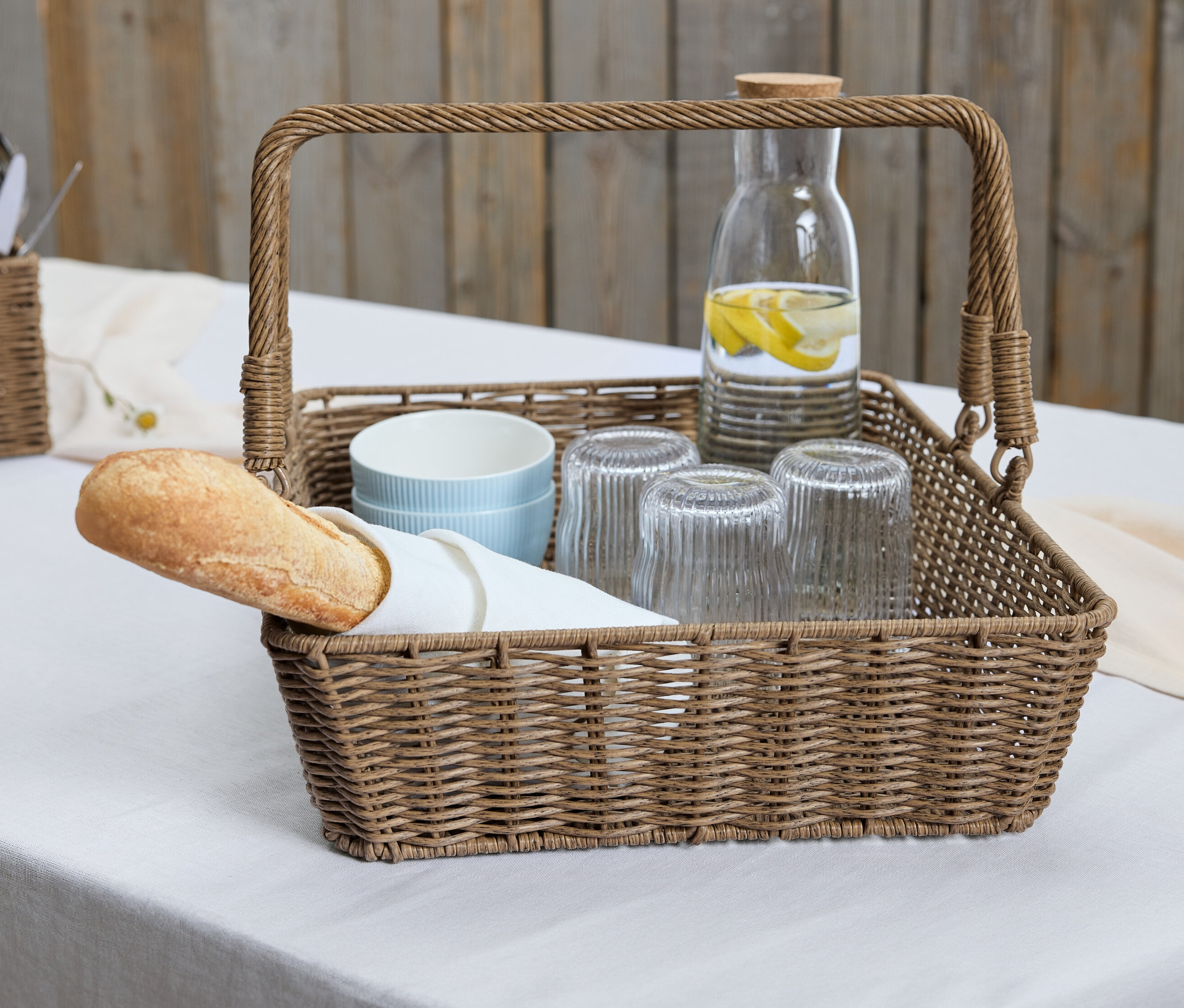 Ein Korbtablett mit Baguette, Gläsern und einer Karaffe mit Zitrone.