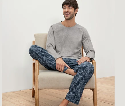 Mann sitzt im Sessel und trägt ein Pyjama-Set.