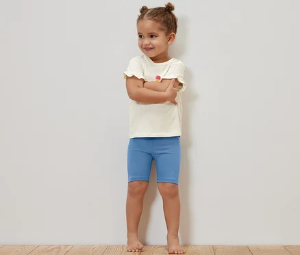Ein Mädchen steht mit verschränkten Armen und trägt blaue Kinder-Radler-Leggings.