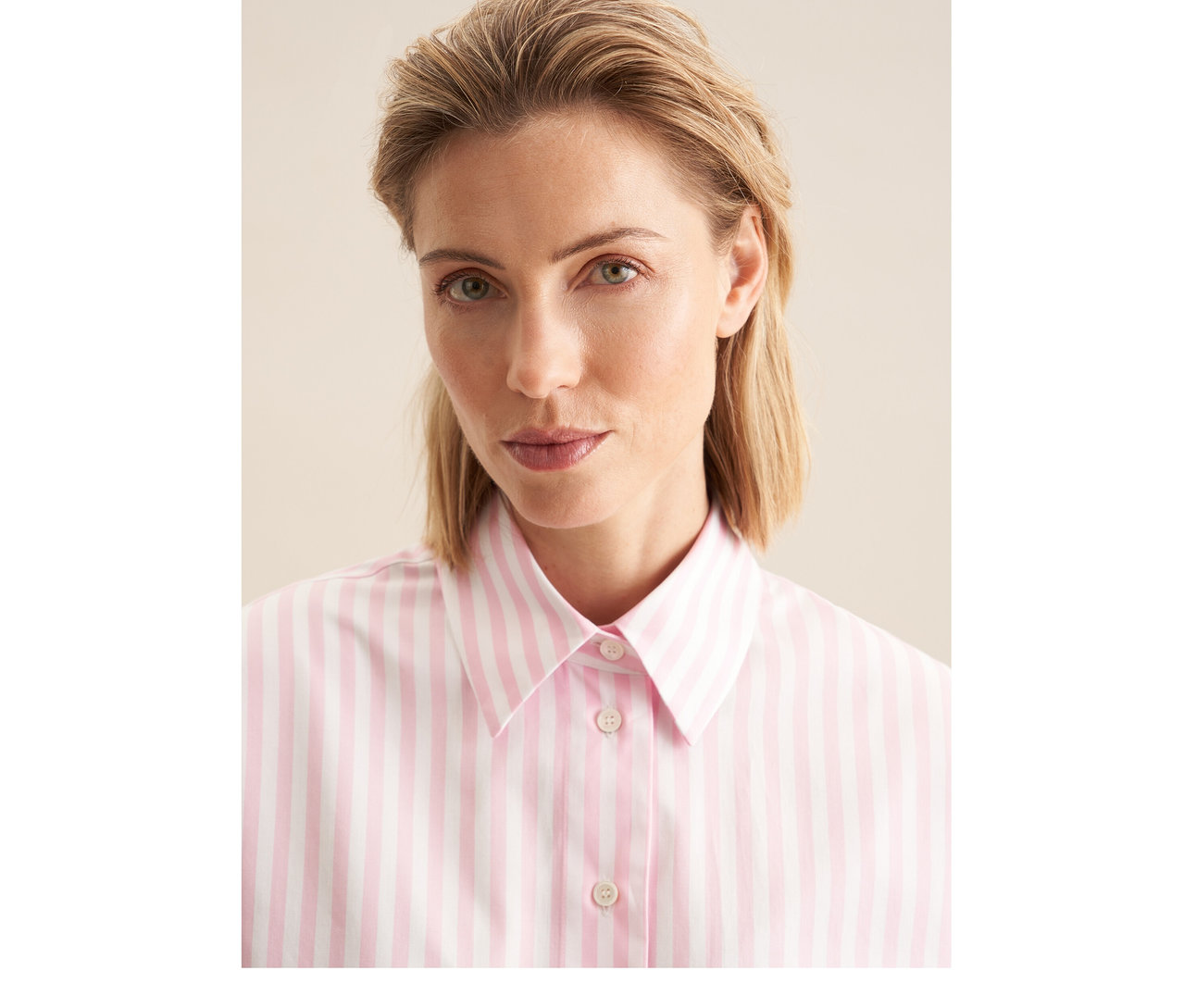 Frau mit blondem Haar trägt eine rosa-weiß gestreifte Seidensticker Oversize Hemdbluse.