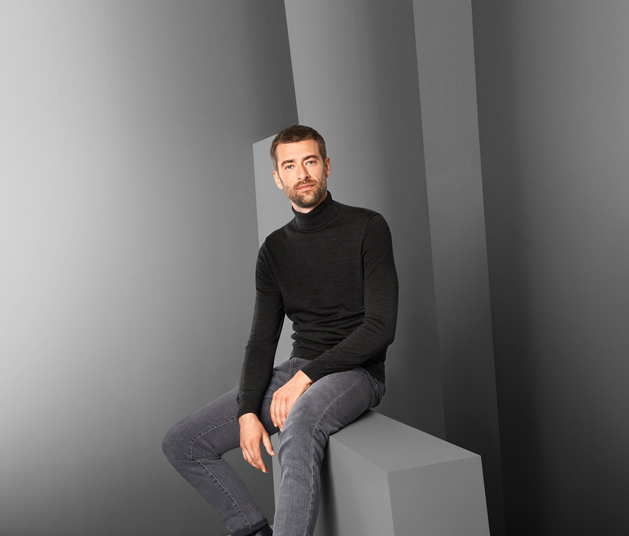 Mann sitzt und trägt einen anthrazitfarbenen Merino-Pullover.