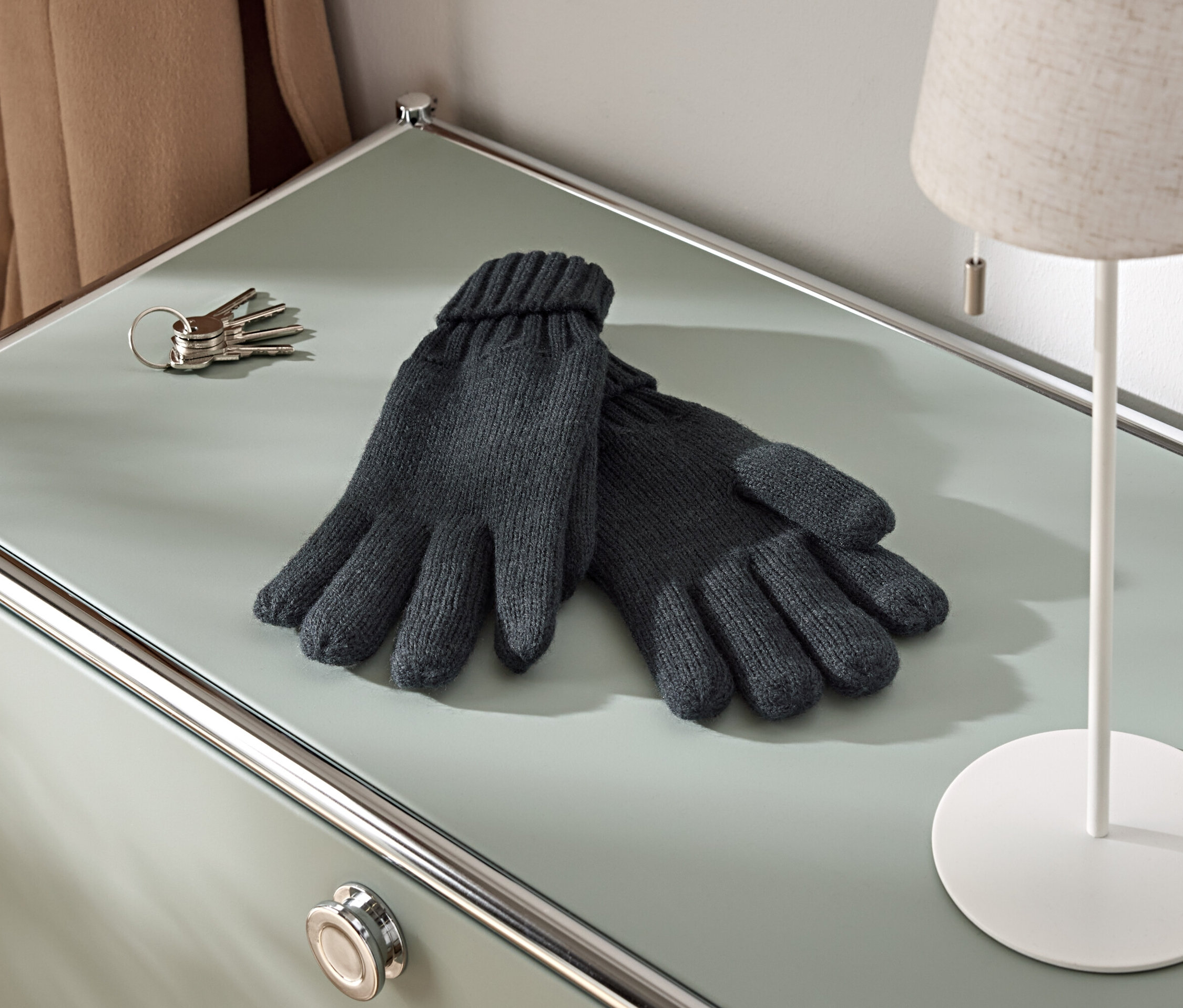 Auf einem Schrank liegen ein Paar Strickhandschuhe, ein Schlüsselbund und eine Lampe.