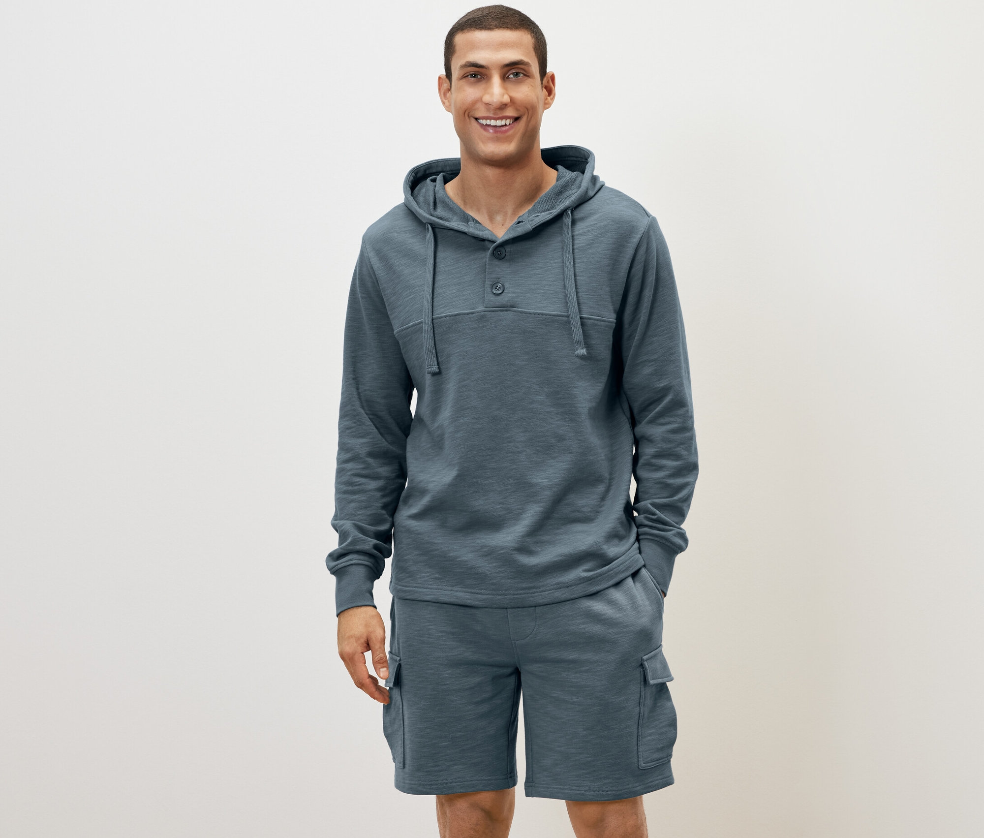 Mann steht und trägt einen blauen Hoodie und Shorts.