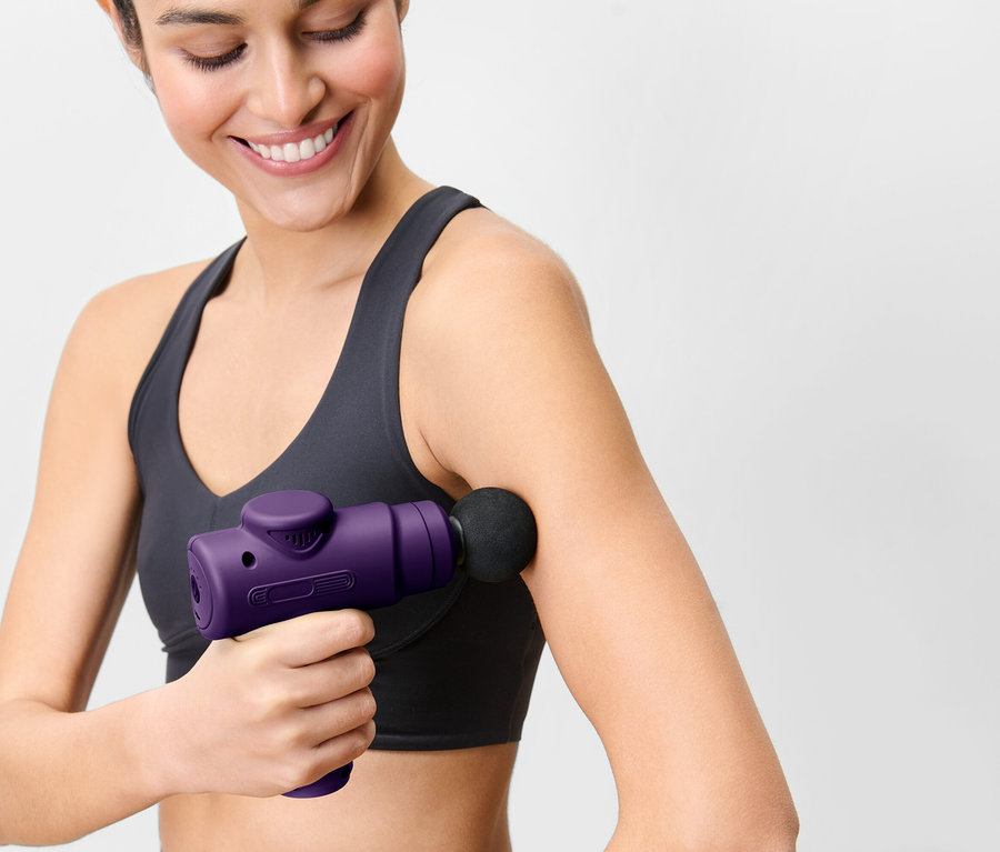 Frau benutzt eine violette Massagepistole am Arm.