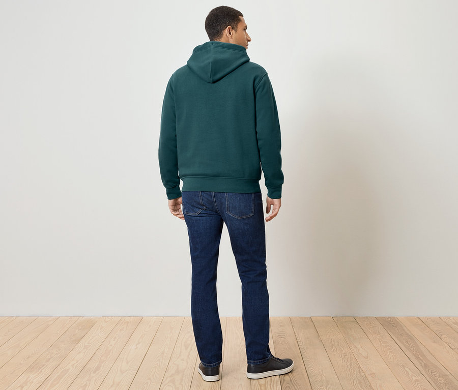 Ein Mann mit dem Rücken zur Kamera trägt einen dunkelgrünen Hoodie, Jeans und Turnschuhe.