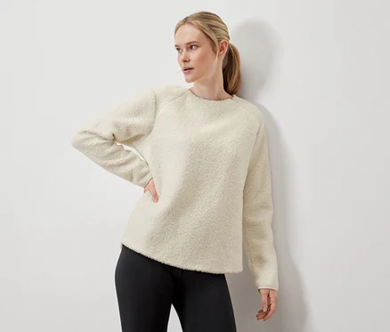 Frau posiert in cremefarbenem Pullover und schwarzen Leggings.