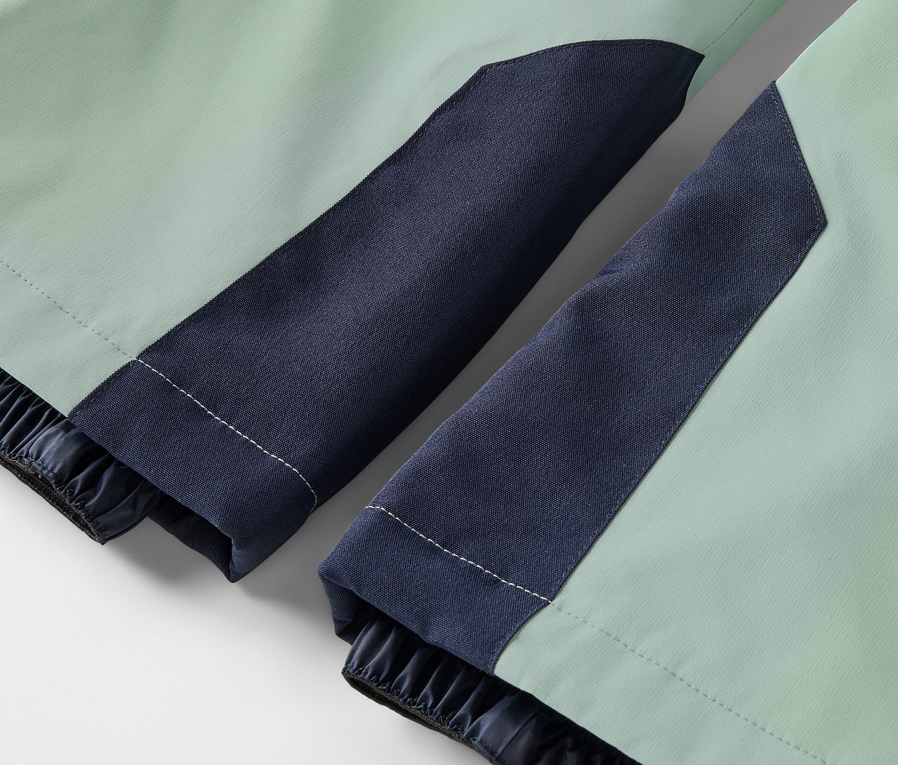 Detailaufnahme einer hellgrünen Jacke mit dunkelblauen Ärmeln und elastischen Bündchen.