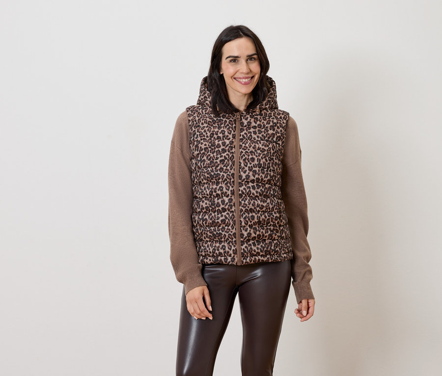Frau posiert in einer braunen Weste mit Kapuze und Tiermuster und braunen Lederhosen.
