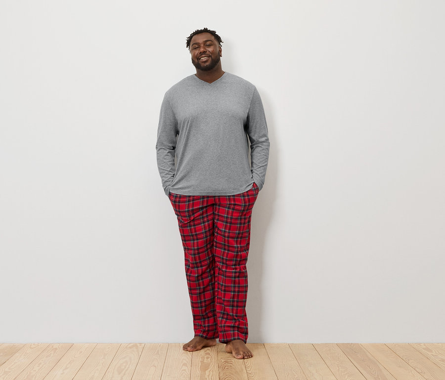 Ein Afroamerikaner steht mit den Händen in den Hosentaschen und trägt ein graues Langarmshirt und eine rot karierte Pyjamahose.